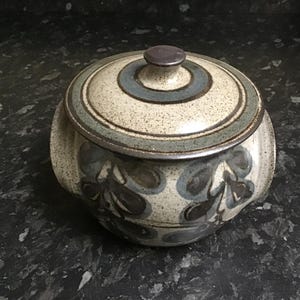May include: A ceramic casserole dish with a lid. The dish is decorated with a brown, blue and white floral pattern. The lid has a brown knob.