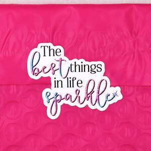 Op de afbeelding: Een roze bubbelenveloppe met een sticker waarop in een kleurrijk, glitterend lettertype "The best things in life sparkle" staat.