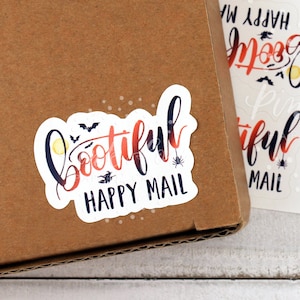 以下が含まれることがあります： ハロウィンをテーマにした黒とオレンジのフォントで「Bootiful Happy Mail」というテキストが書かれた、白いステッカー用紙のシート。ステッカーには、コウモリ、クモ、月が描かれている。