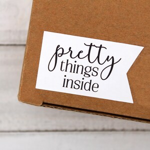 May include: A brown cardboard box with a white label that says "pretty things inside".
