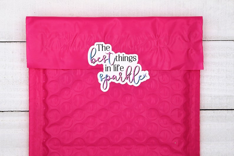Op de afbeelding: Een roze bubbelenveloppe met een sticker waarop in een kleurrijk, glitterend lettertype "The best things in life sparkle" staat.