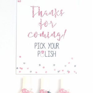 May include: A white card with pink glitter text that says "Thanks for coming! Pick your polish" with a pink diamond ring icon. Three small bottles of nail polish with pink glitter heart shaped tags that say "Made thanks from the bride-to-be".