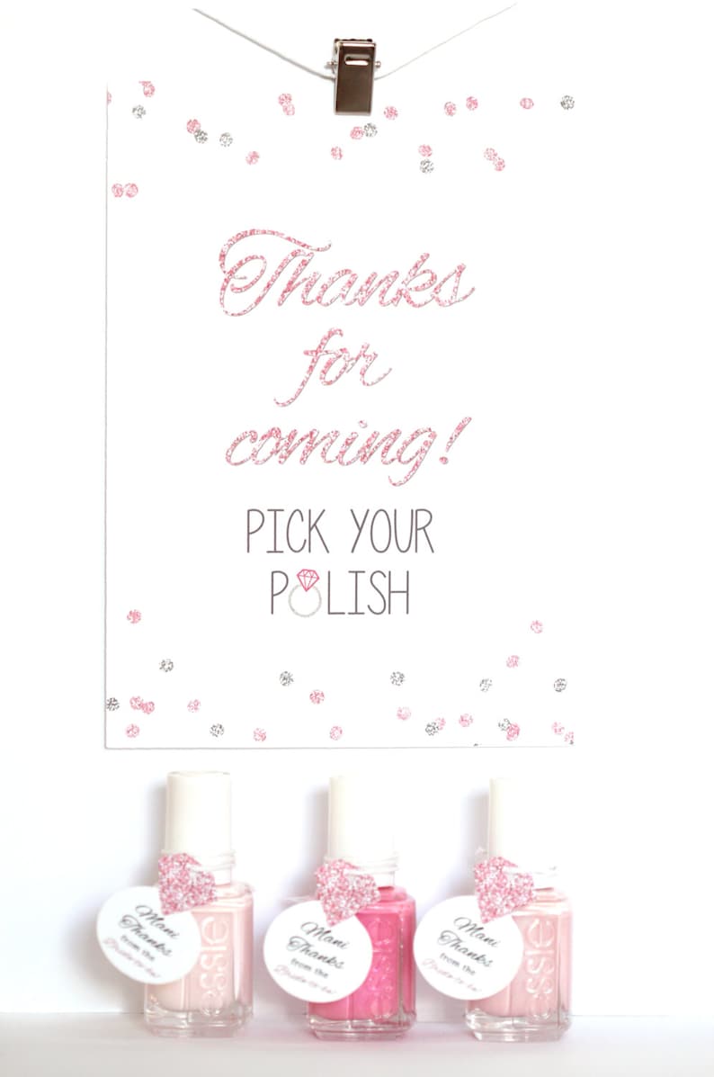 May include: A white card with pink glitter text that reads "Thanks for coming! Pick your polish" with a pink diamond ring icon. Three small bottles of nail polish with pink glitter heart tags that read "Mani Thanks from the Bride" are displayed below the card.