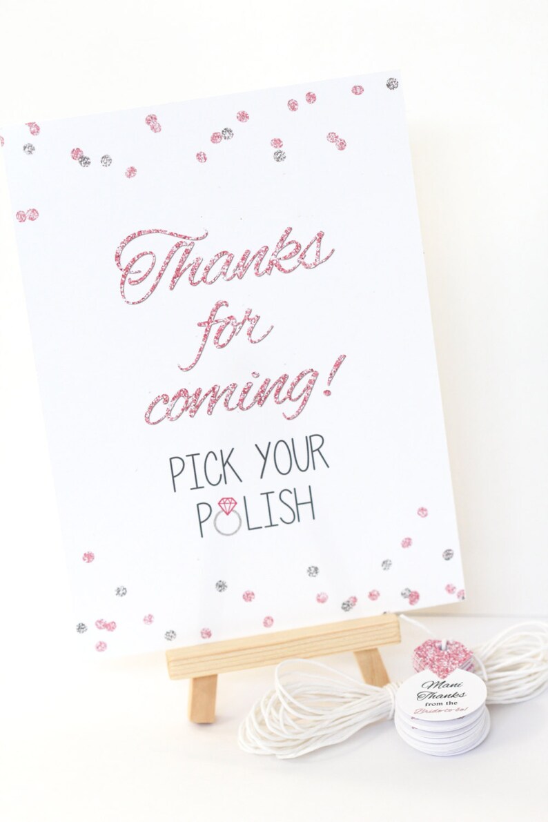 May include: A white sign with pink glitter accents reads "Thanks for coming! Pick your polish" with a pink diamond ring icon. The sign is on a small wooden easel. There are small round white tags with pink glitter accents that say "Mani Thanks from the Bride-to-be".