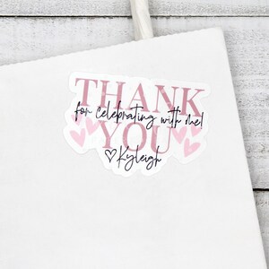 May include: Pink thank you sticker with the text "Thank you for celebrating with me!" and "Kaleigh" with pink hearts around the text.