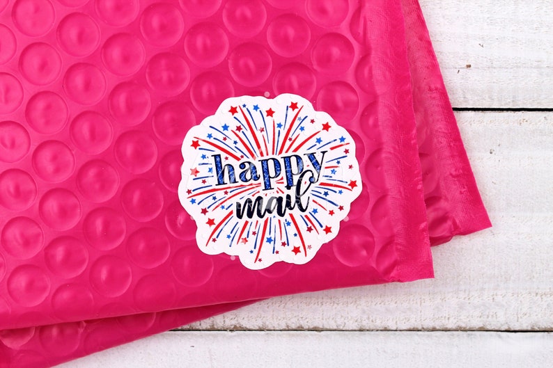 Puede incluir: Un sobre de burbujas rosa con una pegatina blanca que dice "happy mail" con fuegos artificiales rojo, blanco y azul.