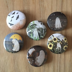 May include: Six round pinback buttons with whimsical ghost illustrations. Each button features a different scene: birds in the sky, a ghost in a jungle, a ghost under the stars, a ghost with an umbrella, a ghost in a library, and a ghost in a sunflower field.