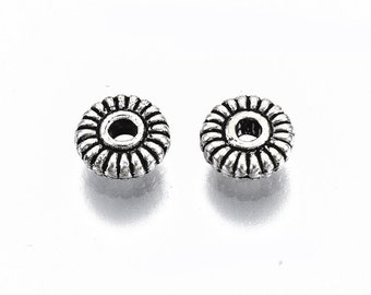 May include: Two silver metal spacer beads with a decorative, circular design. The beads have a hole in the center for stringing.