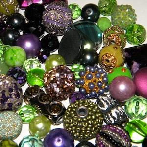 May include: A collection of assorted beads in various shapes, sizes, and textures, featuring a color palette of deep purple, vibrant lime green, black, and metallic gold. The beads include faceted glass, smooth pearls, and intricate metal-encrusted designs.