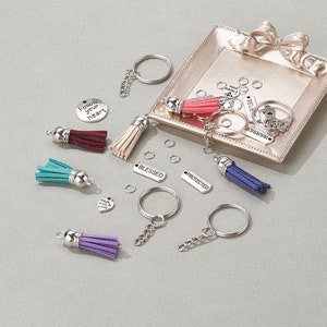 May include: An assortment of keychains and keychain components. The keychains feature colorful tassels in teal, purple, burgundy, and beige. Silver-toned key rings, charms with text like "Follow your heart", and small metal rings are also included.