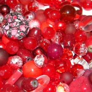 Peut inclure: Un grand assortiment de perles rouges de formes, tailles et textures vari&eacute;es. Les perles sont en verre, en plastique et en d'autres mat&eacute;riaux.