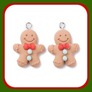 May include: Two gingerbread man charms with red bow ties and white buttons. The charms are made of brown, red, and white polymer clay and have silver jump rings.