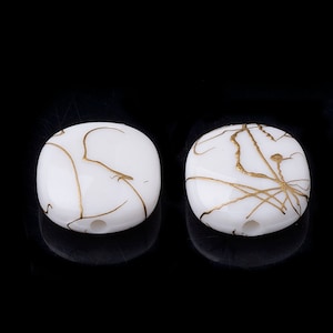 May include: Two white square beads with gold marbling. The beads have a hole in the center for stringing.