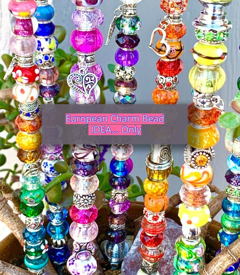 May include: Multiple vertical metal rods adorned with colorful glass and metal beads in various shapes and textures. Some beads feature floral patterns, glitter, or heart-shaped charms. A central text overlay reads: European Charm Bead IDEA... Only.