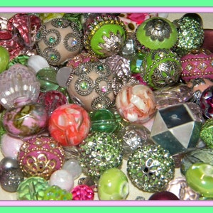 May include: A collection of colorful and patterned beads, including green, pink, white, and brown. The beads are made of various materials, such as glass, plastic, and metal. Some beads have intricate designs, while others are simple and elegant.