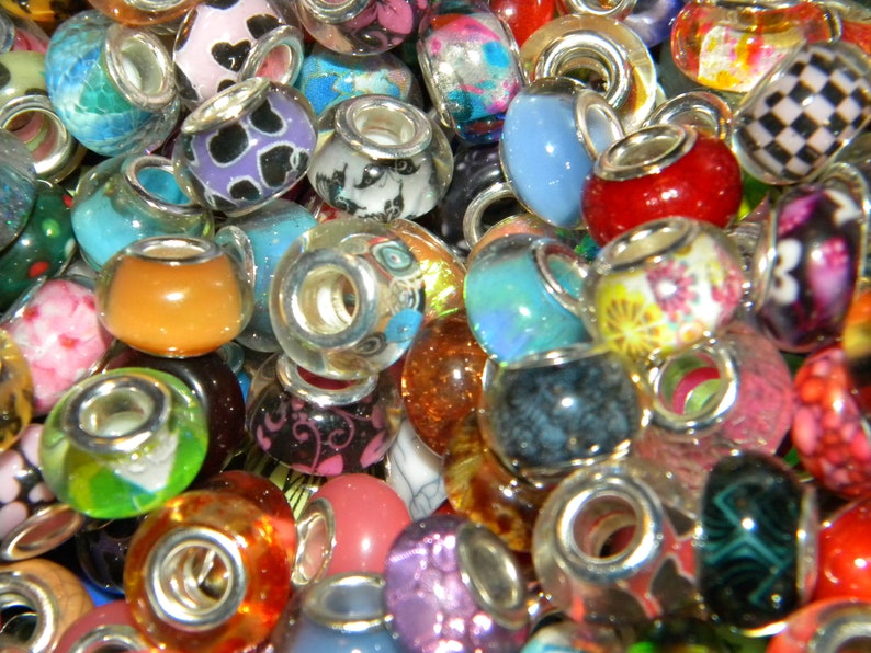 May include: A collection of colorful glass beads with silver-toned metal cores. The beads feature various designs, including floral patterns, animal prints, and solid colors like red, blue, and orange. These decorative beads are suitable for jewelry making.