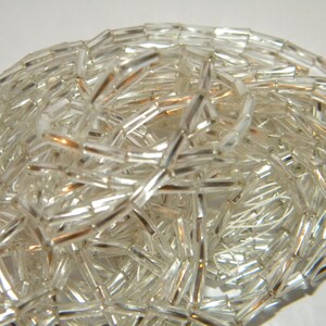 May include: A strand of clear glass beads with a silver iridescent finish. The beads are long and narrow, resembling small tubes.