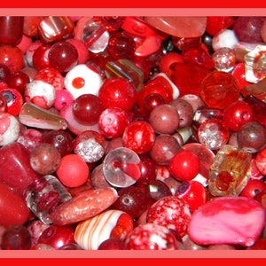 May include: A large assortment of red, pink, and white beads. The beads are made of glass, plastic, and stone. They are perfect for jewelry making or crafting.