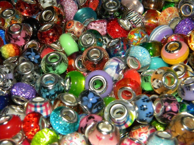 May include: A collection of colorful charm beads with various designs and textures. The beads are made of glass and feature patterns like floral, glitter, and stripes. Each bead has a silver-toned core, creating a vibrant and eye-catching assortment.