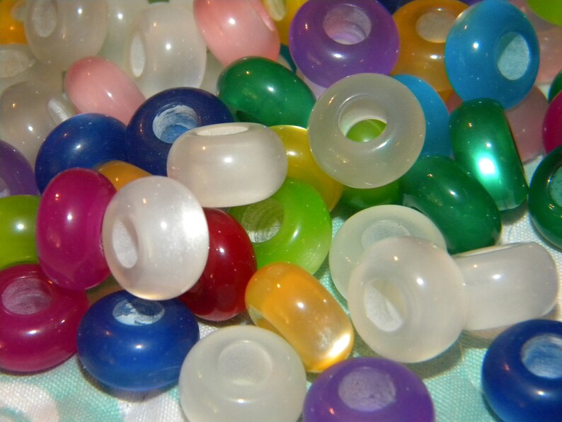 May include: A collection of round, smooth, translucent beads in a variety of vibrant colors including white, blue, green, yellow, red, purple, and pink. Each bead features a central hole, creating a uniform shape across the assortment.