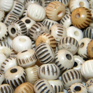 May include: A collection of white and cream-colored bone beads with black stripes. The beads are round and have a hole in the center. They are perfect for making jewelry or other crafts.