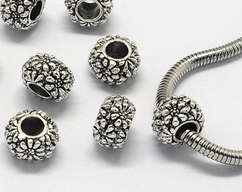 Könnte beinhalten: Silberfarbene Metallperlen mit Blumenmuster. Die Perlen haben ein Loch in der Mitte zum Einfädeln auf ein Armband oder eine Halskette.