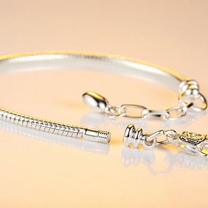 May include: A silver snake chain bracelet with a clasp closure. The bracelet is open and the clasp is visible.