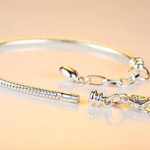 May include: A silver bracelet with a snake chain design, featuring a lobster clasp and an adjustable chain. The bracelet is unclasped, showing the separate components. The jewelry is displayed on a light-colored surface.