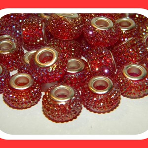 May include: A close-up of a pile of red rhinestone beads with silver metal accents. The beads are round and have a sparkly finish.