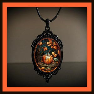 May include: An oval pendant necklace featuring a black metal frame with an intricate filigree border. The center displays a stained glass style illustration of an orange pumpkin surrounded by brown tree branches and yellow autumn leaves.