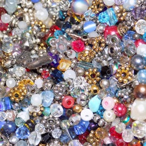 May include: A close-up view of a collection of beads in various shapes, sizes, and colors. The beads include silver, gold, red, blue, white, and clear. Some beads have a pearl-like appearance, while others are faceted or metallic.