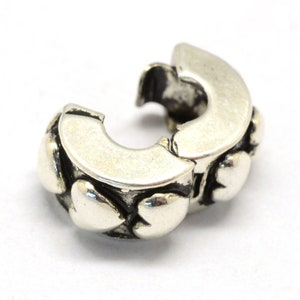 May include: Silver charm bracelet clasp with a heart design. The clasp is made of silver and has a heart-shaped design. The clasp is open and ready to be attached to a bracelet.