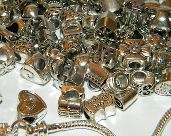 Könnte beinhalten: Eine Sammlung von silbernen Charms mit verschiedenen Designs, darunter Herzen, Blumen und Wörter wie "Love" und "Brave". Die Charms sind für die Verwendung an einem Charms-Armband gedacht.