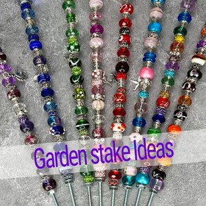 May include: A collection of colorful beaded garden stakes. Each stake features a variety of beads in different colors and patterns, including clear, purple, blue, green, red, pink, orange, and black. The text "Garden stake Ideas" is overlaid on the image.