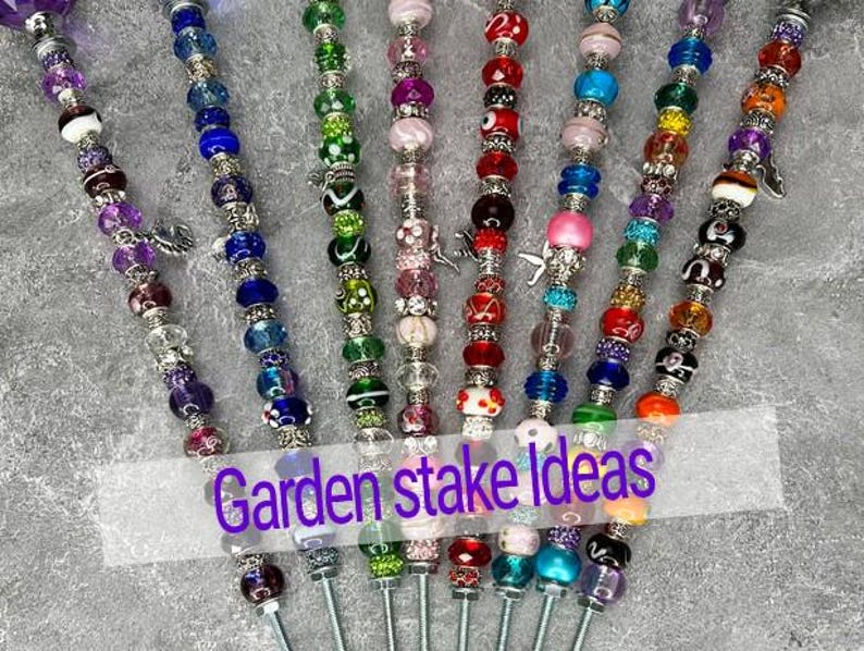 May include: A collection of colorful beaded garden stakes. Each stake features a variety of beads in different colors and patterns, including clear, purple, blue, green, red, pink, orange, and black. The text "Garden stake Ideas" is overlaid on the image.