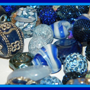 May include: A collection of assorted beads in various shades of blue, including dark blue spheres with silver floral patterns, light blue crackle glass beads, blue and white swirled heart-shaped beads, and dark blue textured pavé-style beads.