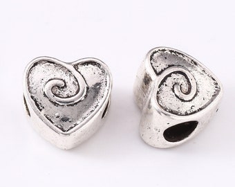 May include: Two heart-shaped beads with a metallic silver finish and a dark, weathered texture. Each bead features a raised spiral design centered on the front face and a horizontal hole running through the side for threading onto a cord or wire.