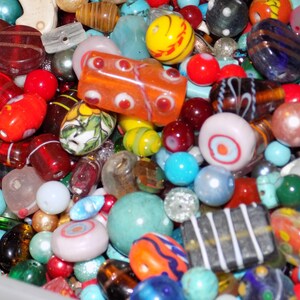 May include: A large collection of assorted loose beads in various shapes, sizes, and colors. The mix includes round, cylindrical, and rectangular glass beads in shades of red, blue, green, yellow, orange, and white with striped and floral patterns.