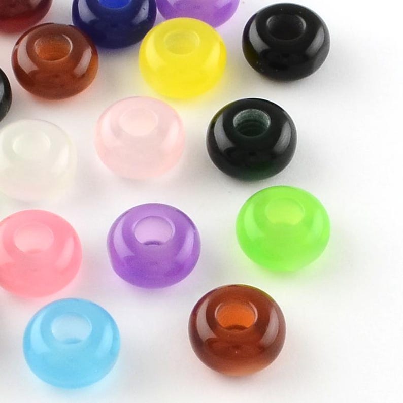 May include: A collection of round, smooth, translucent beads in various colors including yellow, black, brown, pink, purple, green, blue, and white. Each bead features a central hole, creating a uniform shape across the assortment of colors.