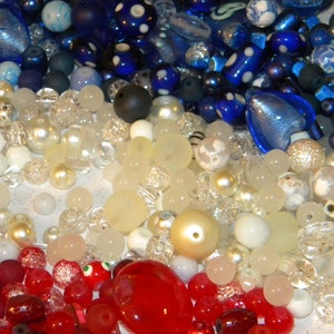 Peut inclure: Une collection de perles de verre color&eacute;es dans des tons de bleu, blanc et rouge. Les perles sont dispos&eacute;es de mani&egrave;re al&eacute;atoire et sont parfaites pour la cr&eacute;ation de bijoux ou d'autres objets d&eacute;coratifs.