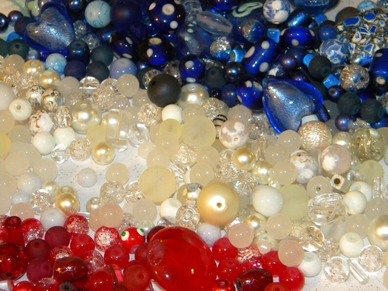 Peut inclure: Une collection de perles de verre color&eacute;es dans des tons de bleu, blanc et rouge. Les perles sont dispos&eacute;es de mani&egrave;re al&eacute;atoire et sont parfaites pour la cr&eacute;ation de bijoux ou d'autres objets d&eacute;coratifs.