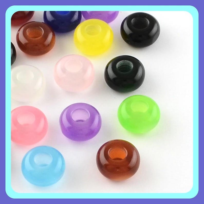 May include: A collection of smooth, round, translucent beads in various colors including yellow, black, blue, pink, purple, green, and brown. Each bead features a central hole, creating a donut-like shape, arranged in a scattered pattern.