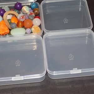 May include: Three square, clear plastic storage containers with hinged lids. One container is filled with a variety of colorful, multi-shaped gemstone beads, including orange, purple, white, and green stones of various sizes and textures.