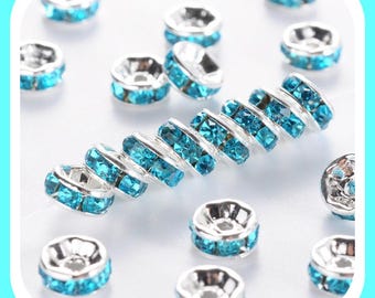 May include: A close-up of a group of silver-toned bead caps with turquoise blue rhinestones. The bead caps are arranged in a circle and are scattered on a white surface.