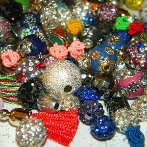 May include: A collection of colorful and patterned beads, including silver, blue, pink, red, and green beads. Some beads have a sparkly finish, while others have a smooth, matte finish. The beads are arranged in a random pattern, creating a visually appealing and diverse assortment.