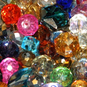 May include: A large assortment of colorful faceted glass beads in various shapes and sizes. The beads are a mix of clear, pink, blue, green, red, and brown.