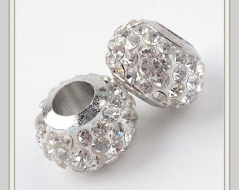 May include: Two silver-toned, rhinestone-studded beads. Each bead has a cylindrical shape with a large central hole. The surface of each bead is covered in small, sparkling rhinestones, giving them a glamorous appearance. The beads are set against a white background.