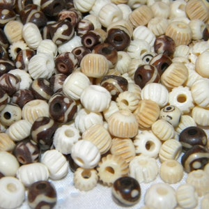 May include: A collection of white and brown bone beads. Some beads have a carved design, while others have a simple round shape.
