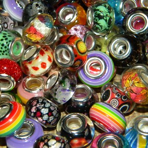 May include: A collection of colorful glass beads with silver-toned metal cores. The beads feature various designs, including floral patterns, polka dots, and rainbow stripes. The beads are in shades of red, green, blue, purple, and orange.