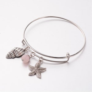 May include: Silver bangle bracelet with a pink bead, a seashell charm, and a starfish charm.
